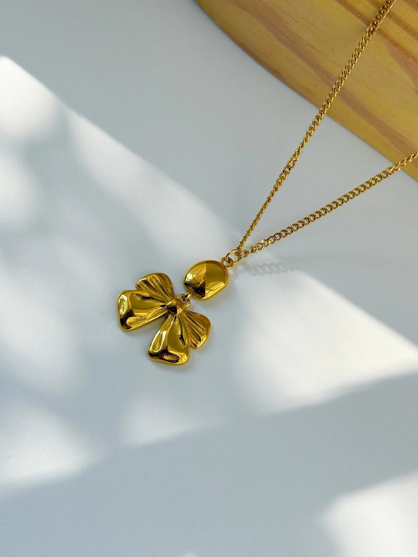 Gold necklace with a leaf-shaped pendant on a white surface