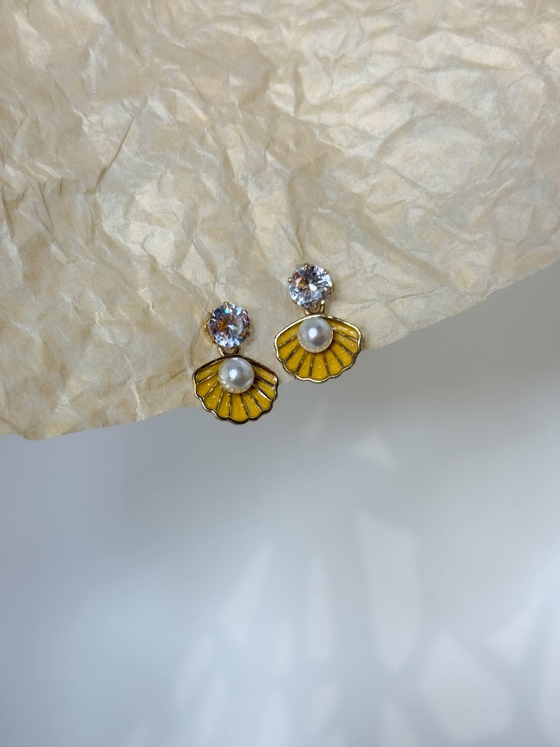 Pair of earrings with yellow and gold floral designs on a textured beige surface.