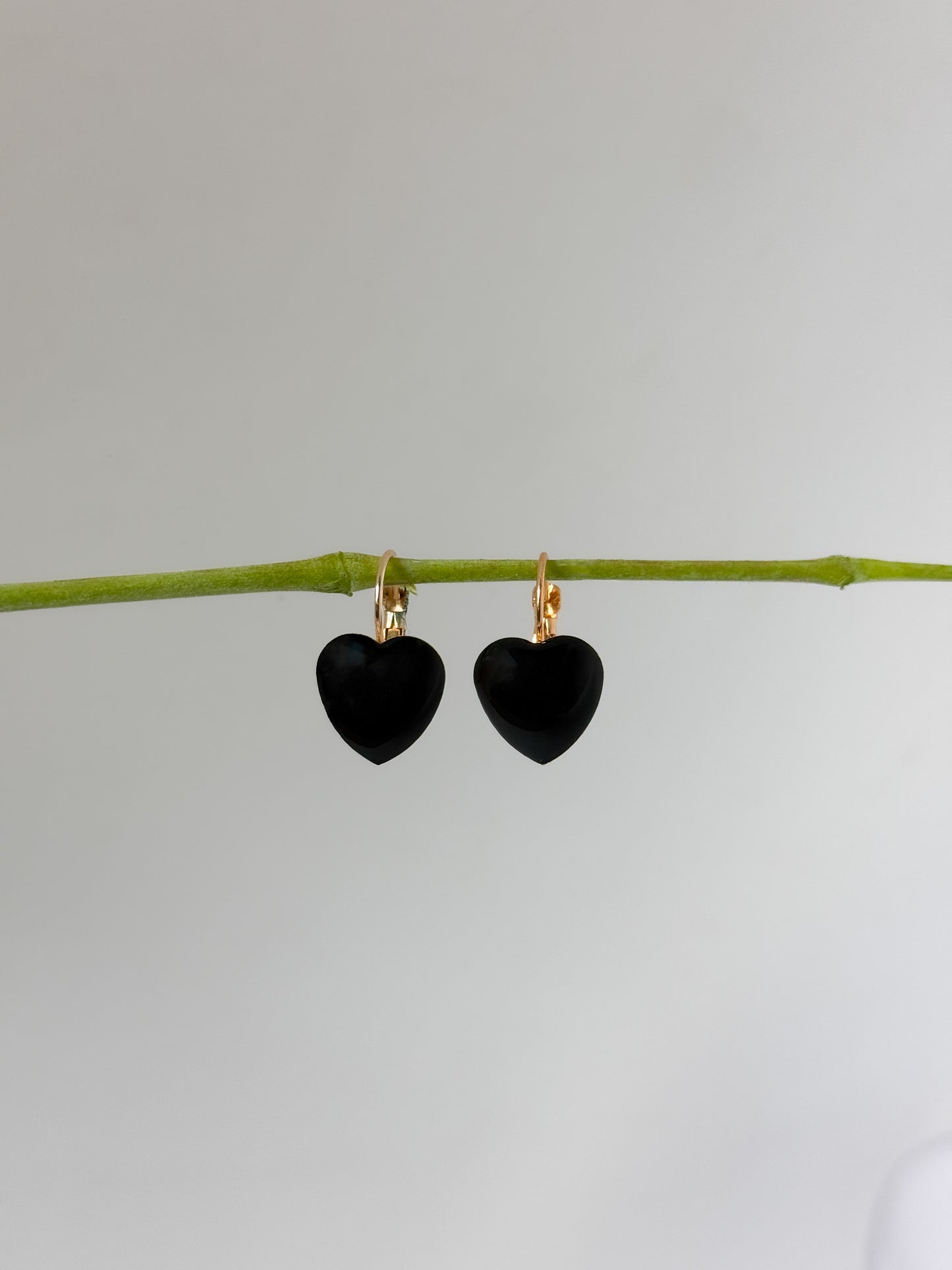 Black heart-shaped earrings on a thin branch against a light gray background