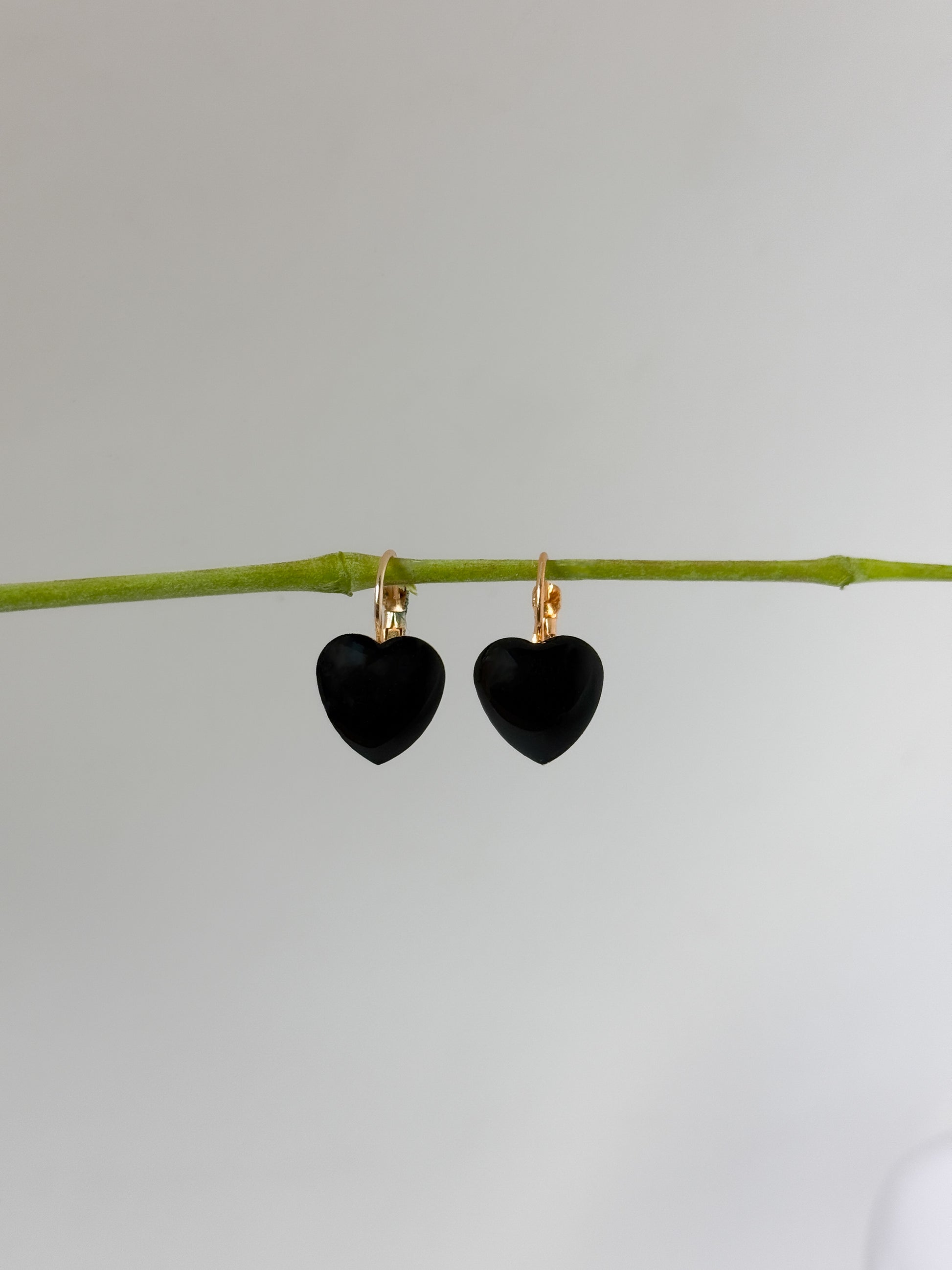 Black heart-shaped earrings on a thin branch against a light gray background