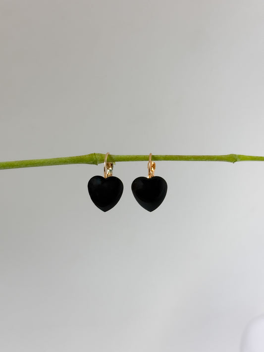 Black heart-shaped earrings on a thin branch against a light gray background
