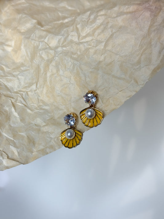 Pair of earrings with yellow floral designs and pearl-like centers on a textured beige surface.