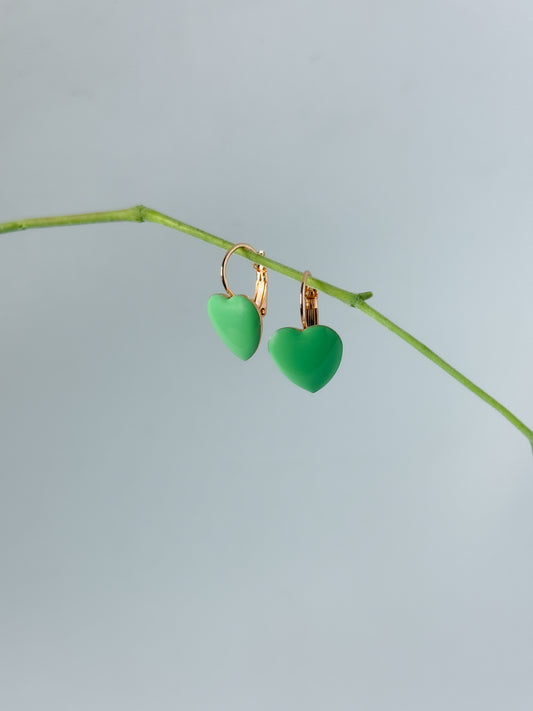 Green heart-shaped earrings on a thin branch against a light blue background