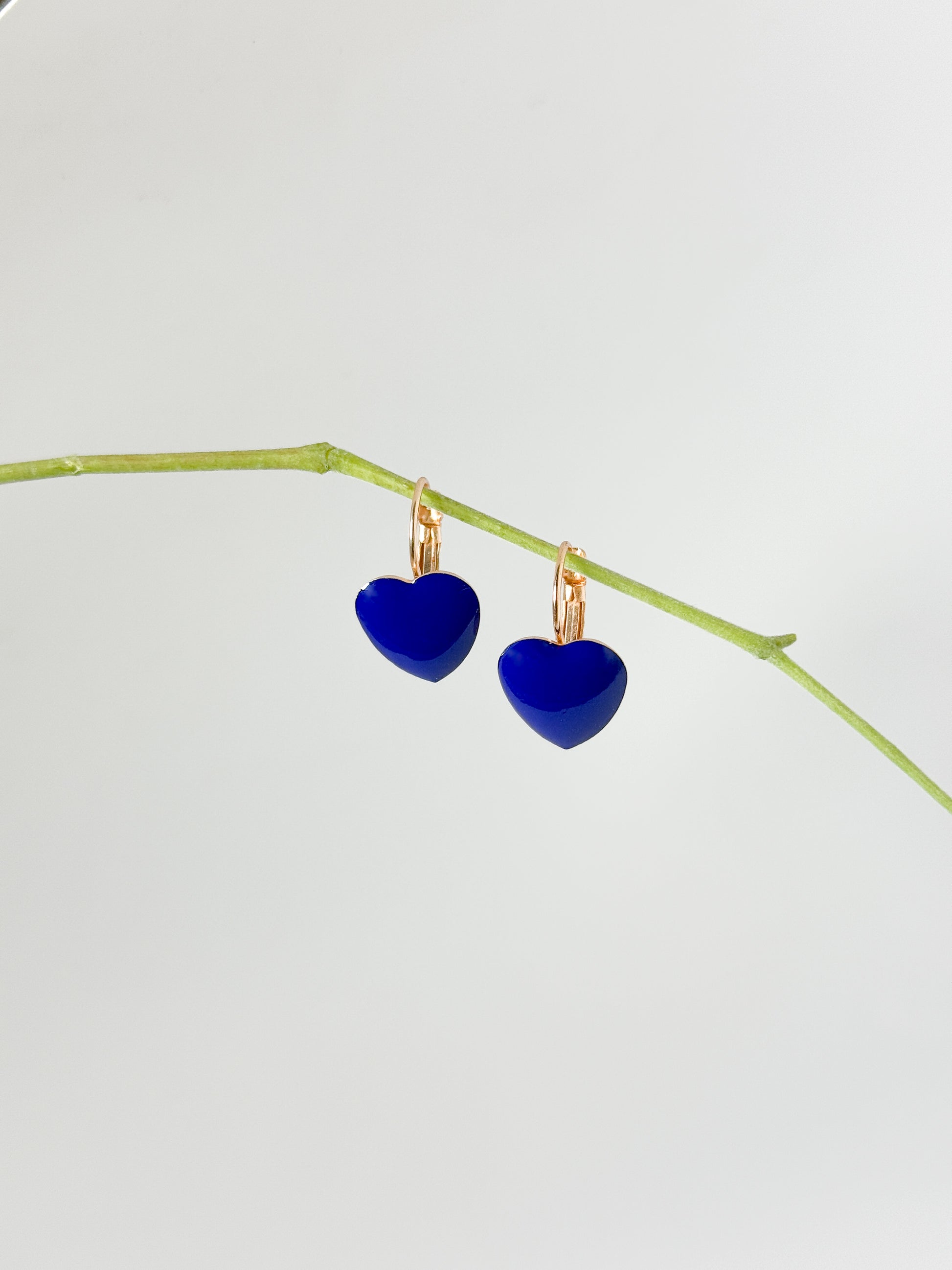 Blue heart-shaped earrings on a thin branch against a light gray background
