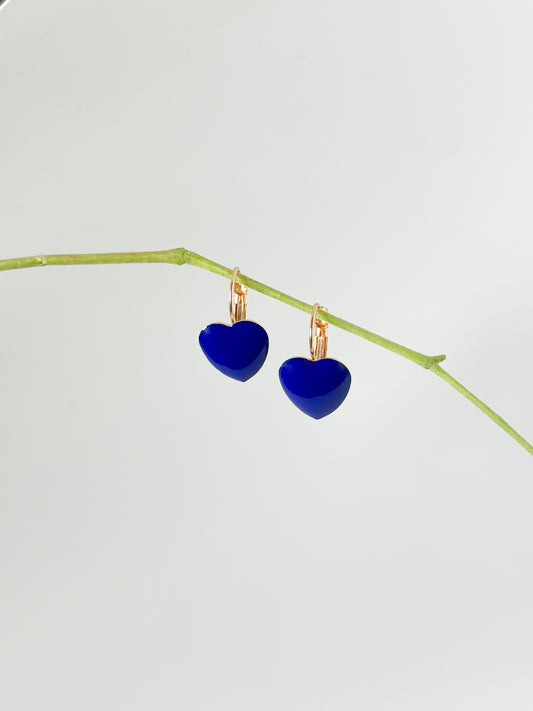 Blue heart-shaped earrings on a thin branch against a light gray background