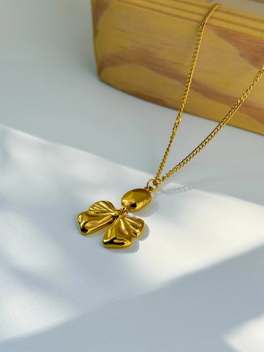 Gold necklace with a leaf-shaped pendant on a white surface with a wooden block in the background.