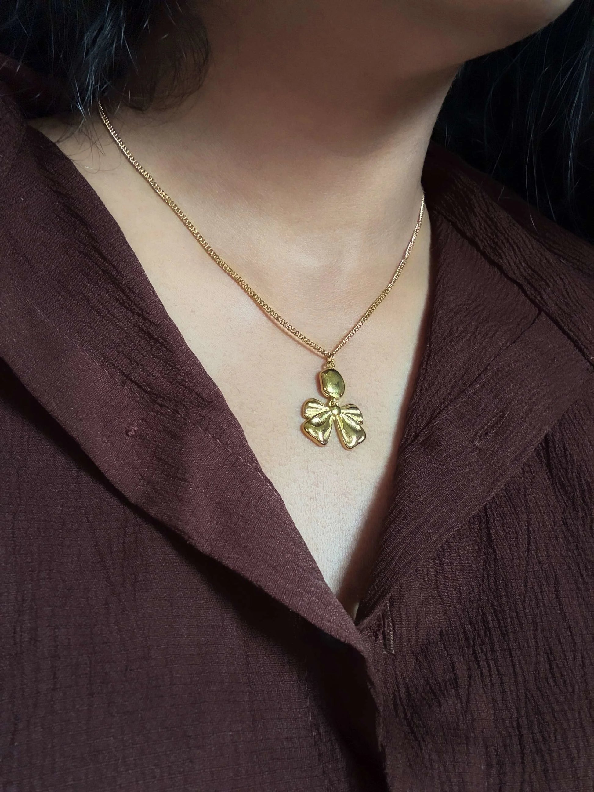 Gold necklace with a leaf pendant worn by a person in a brown garment.