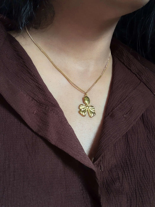 Gold necklace with a leaf pendant worn by a person in a brown garment.
