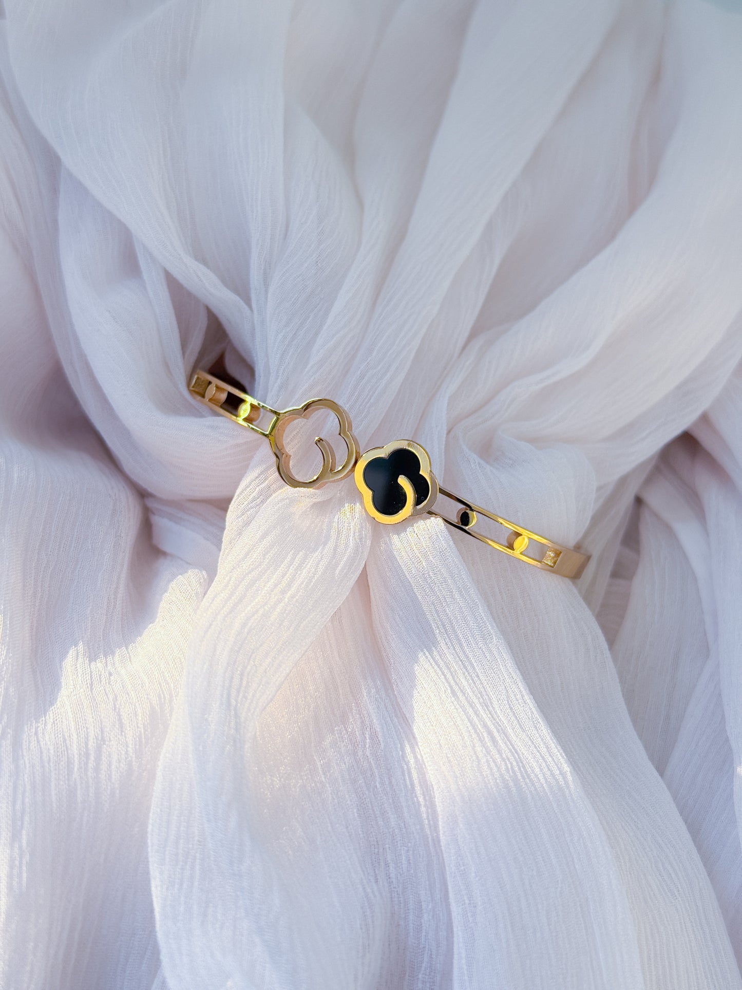 Gold bracelet with a black heart charm on a white fabric background