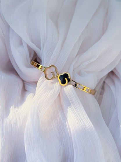 Gold bracelet with a black heart charm on a white fabric background
