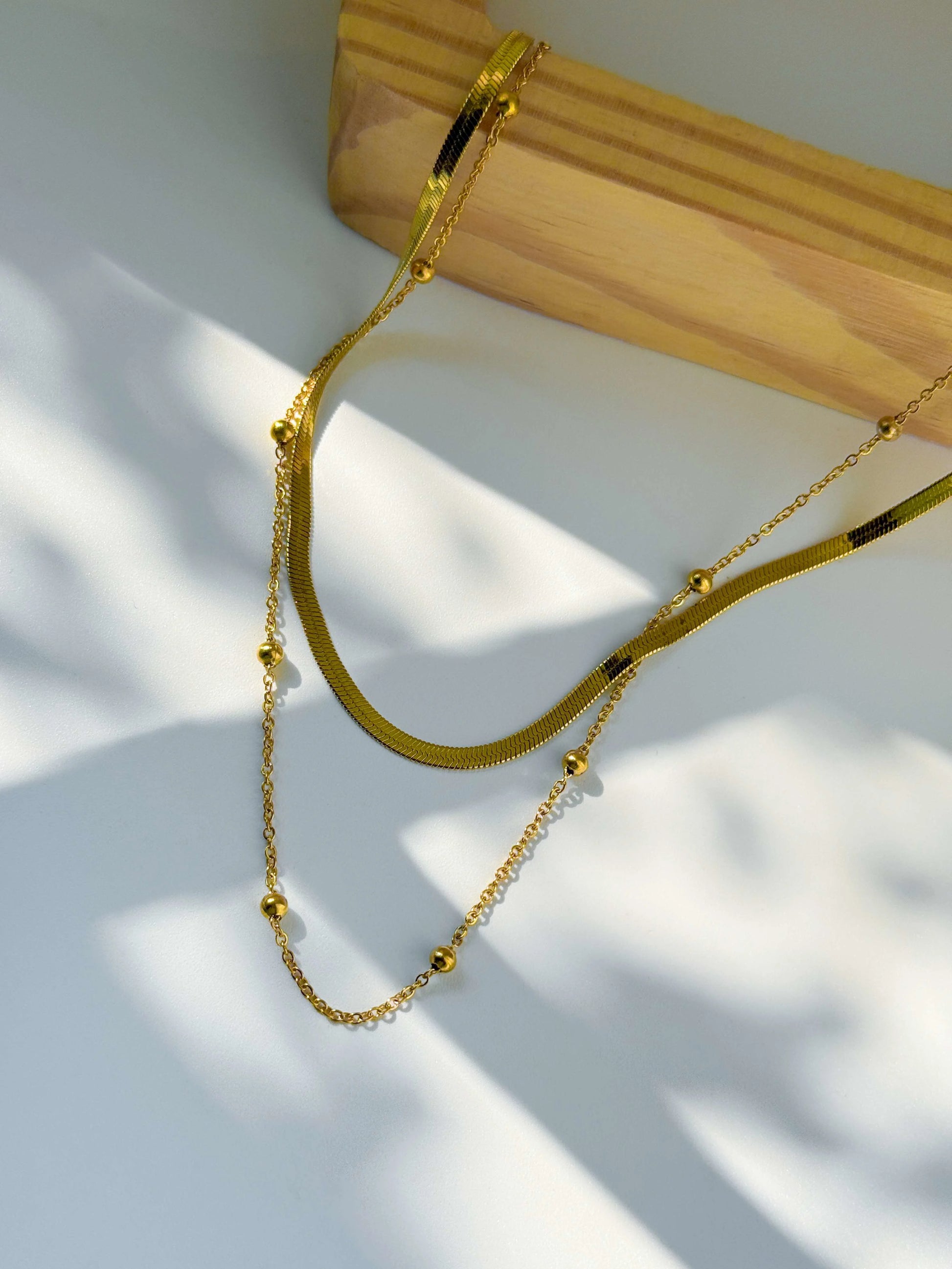 Anti Tarnish double layered Gold necklace on a white surface with a wooden block