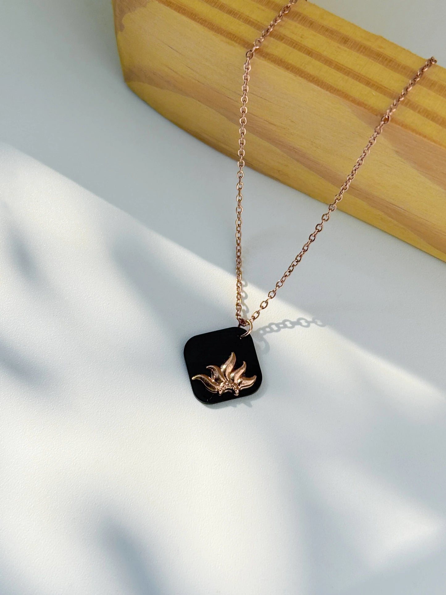 Anti Tarnish Necklace with a black pendant featuring a gold design on a light background with wooden block